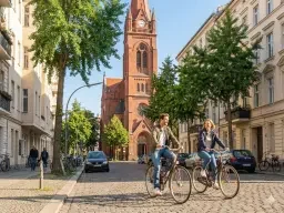 Umgebung der Praxis für Paartherapie Schöneberg Ein Paar fährt mit dem Fahrrad an der Kirche zum Heilsbronnen nahe der Praxis für Paartherapie in Berlin Schöneberg vorbei